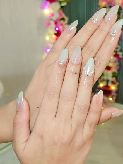 A soft and angelic look with long, pearlescent white stiletto nails. Subtle rhinestone placements near the cuticles add a touch of sophisticated sparkle.