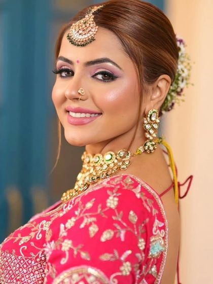 A smiling bride wearing a heavy Kundan choker and maang tikka. The floral hair bun and pink lehenga create a fresh and joyful bridal look.