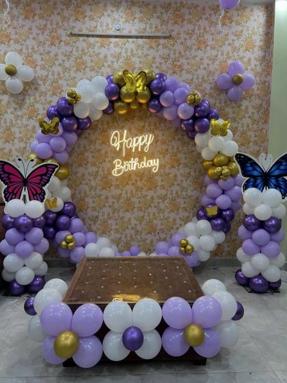 A beautiful butterfly-themed ring decoration for a home party. This setup features a circular balloon arch in purple, white, and gold, with large butterfly cutouts.