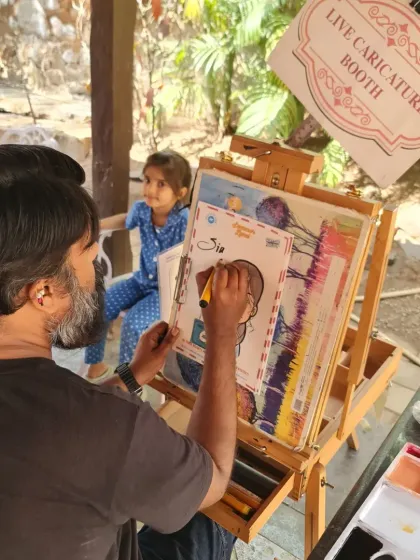 This is my happy place, my live caricature booth. Here I am, focused on capturing a young guest's likeness, with my easel and art supplies ready for the next smiling face.