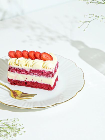 A slice of our Red Velvet and Strawberry cake on a delicate plate, a perfect way to enjoy the last of the strawberry season.