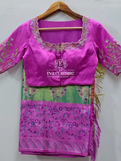 A beautiful saree blouse in magenta with intricate floral embroidery on the back and sleeves. This piece is designed to complement the green and pink saree.