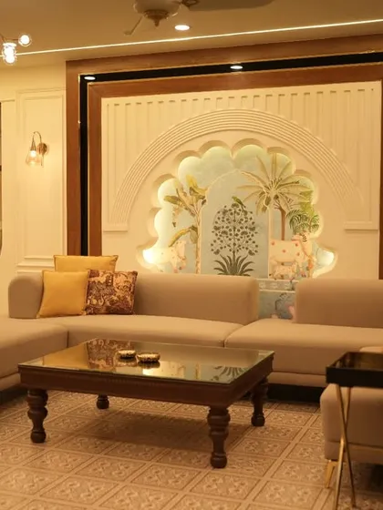 A living room designed with a blend of modern and traditional Indian elements. It features an L-shaped sofa, a classic wooden coffee table, and a stunning arched wall niche with custom artwork.