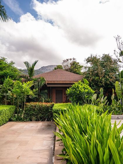 A view of our resort grounds, with manicured hedges and lush greenery framing the path to one of our private bungalows, with Nandi Hills in the distance.