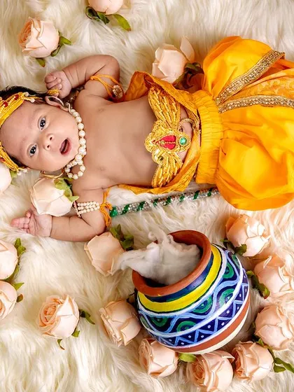 This wide shot shows the full setup for our Krishna theme, with the baby lying on a soft fur blanket surrounded by roses and his colorful matki.