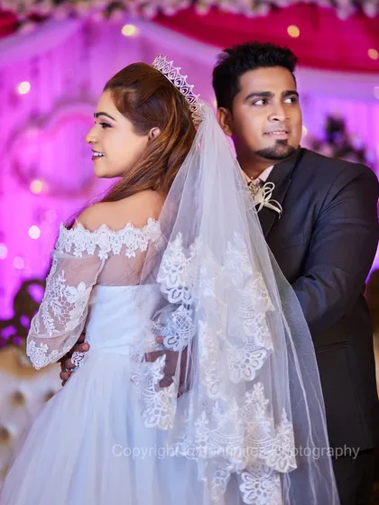 This portrait captures the elegance of a Christian wedding. The bride's lace gown and flowing veil create a beautiful silhouette as she poses with her groom.