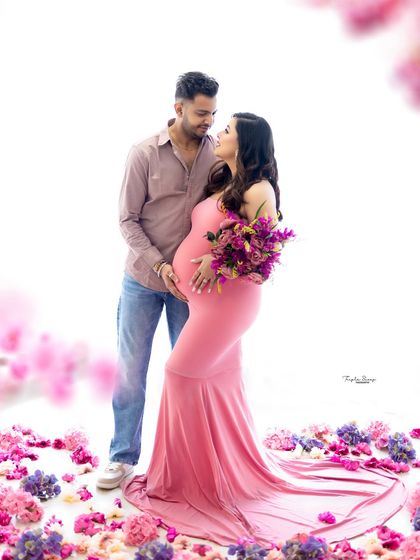A beautifully framed shot using foreground flowers to add depth. This pose highlights the couple's loving gaze and the mom-to-be's beautiful baby bump.