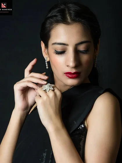 A classic beauty shot where less is more. The focus is on the model's serene expression, highlighted by the dramatic contrast of dark background, red lips, and delicate jewelry. This is about capturing quiet intensity.