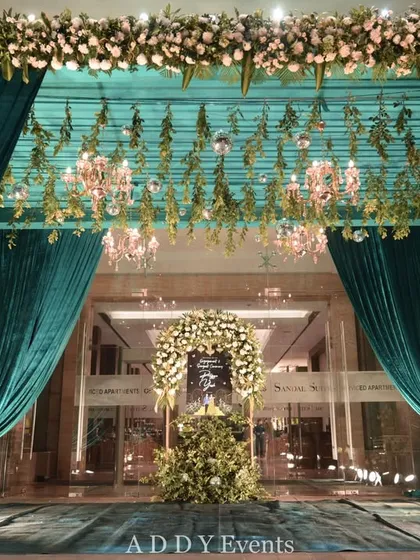 A grand entrance framed by lush teal velvet curtains and a ceiling of hanging florals and chandeliers. This opulent design creates a sense of occasion and luxury, ideal for a high-profile corporate gala or partner event.