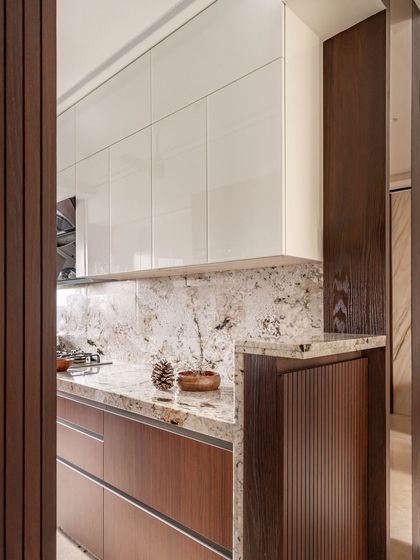 The kitchen combines functionality with elegance. It features a black and white granite countertop, sleek wooden-finished lower drawers, and white glass-finished upper cupboards for ample, stylish storage.