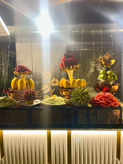 A beautifully lit fruit station, featuring an assortment of fruits like grapes, melons, and berries, presented in elegant glassware.