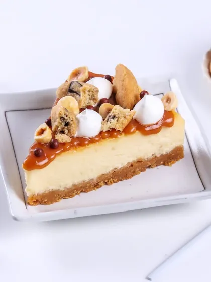 A slice of the Caramel Seasalt Cheesecake, showing off all the delicious toppings. It's a party of textures with cookie chunks, hazelnuts, and smooth caramel.