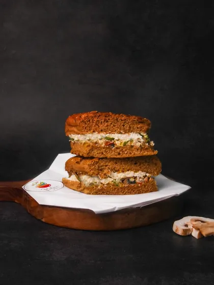 A multigrain sandwich with a creamy filling, stacked on a wooden board against a dark background. The moody lighting creates a sophisticated look for a simple sandwich.