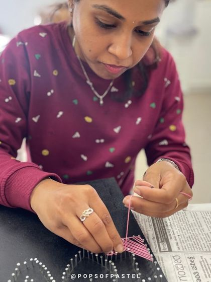 A close-up of hands weaving pink string to form a letter, a key part of creating a personalized nameplate.