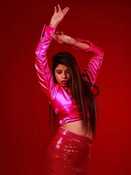 A dynamic pose against a vibrant red backdrop. The movement in her arms and the energy of the satin and sequins create a portrait that is full of life and attitude.