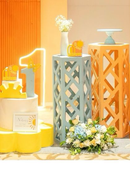 A close-up of the 'Here Comes the Sun' party decor, featuring a light-up '1', decorative pedestals, and a sunshine-themed cake.