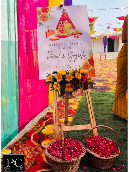 A beautiful welcome easel for a Haldi ceremony, featuring custom graphics of a bride and groom, along with baskets of fresh petals for the guests.