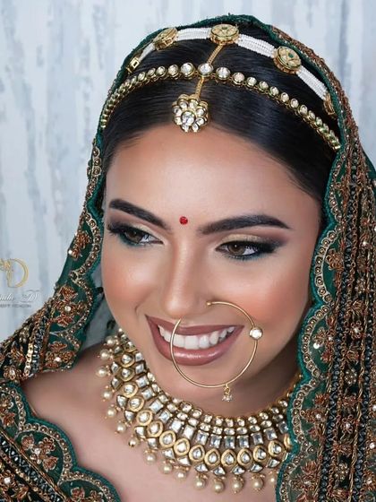An exquisite bridal transformation featuring a stunning green lehenga and intricate jewelry. The makeup is glamorous yet refined, with a focus on creating a radiant and smiling bride.