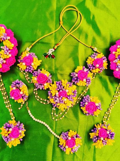 A vibrant and colorful floral jewelry set perfect for a lively Mehendi or Haldi function. This set features a beautiful combination of pink, yellow, and purple flowers, and includes a necklace, hathphools, earrings, and a maang tikka.