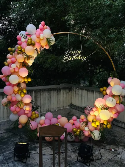 This popular circular ring backdrop is great for any celebration. Here, it's decorated with a dense arch of pink, peach, and gold balloons for a birthday party, creating a beautiful photo opportunity on a terrace.