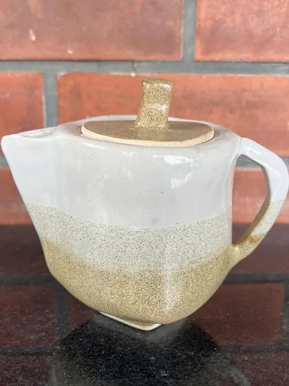 A uniquely shaped hand-built teapot with a clean, modern aesthetic, featuring a two-tone glaze.