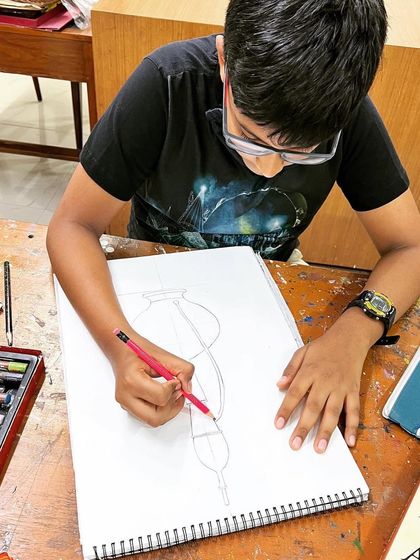 A student carefully drawing a still life of vases, practicing foundational skills of observation and line control.