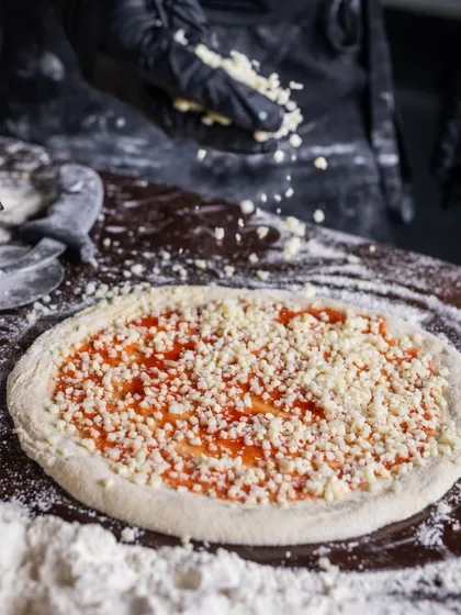 Get your pizza fix at Camillo's. Here, a pizza is being generously topped with cheese before baking.