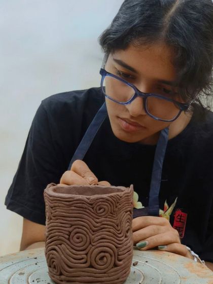 This student is using the coiling technique to create a textured pattern on her pot. By rolling out and applying thin coils of clay, she can build up unique surface designs.