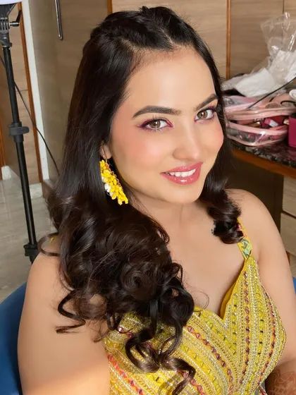 A stunning Haldi look with a pop of color on the eyes. The pink eyeshadow and fresh, dewy skin perfectly complement the yellow outfit and floral earrings.