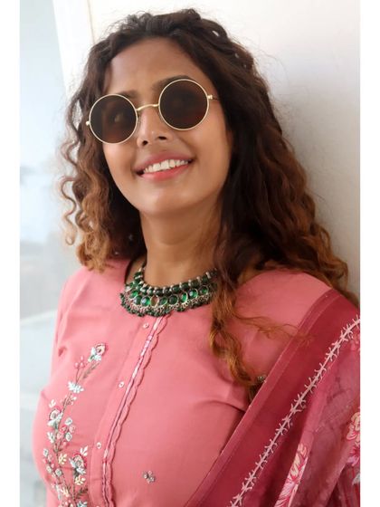 A closer look at the accessory pairing. The contrast between the pink suit and the green necklace adds a unique and personal touch to the outfit.