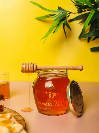 A bright and cheerful shot of Acacia Honey against a yellow background. The dripping honey adds a sense of deliciousness and movement.
