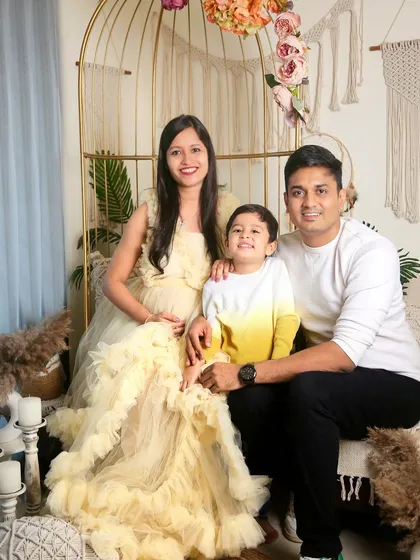 A beautiful family portrait taken during a maternity session. The expecting mother is glowing in a ruffled yellow gown, seated with her husband and son.