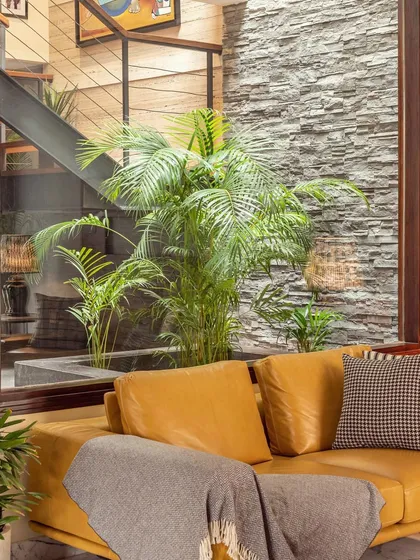 Integrating greenery and natural materials is a key part of my design process. Here, an indoor court with a stone wall provides a beautiful natural backdrop for a stunning yellow top-grain leather sofa.