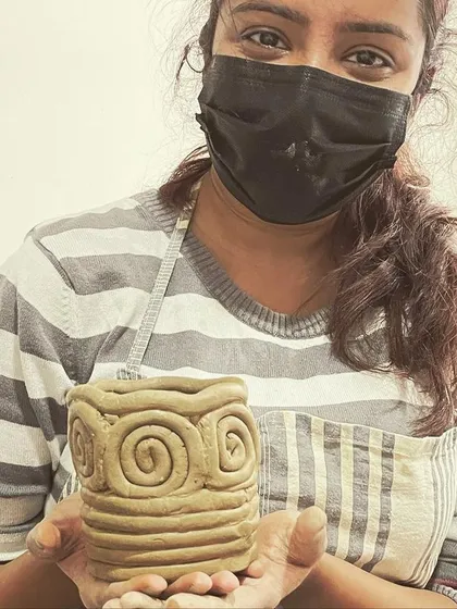 A student proudly displays their coiled pot with a spiral design, a result of our hand-building workshop.