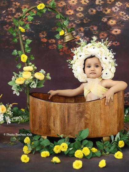 A wider view of the yellow floral bath setup, with a vine-covered shower prop and flowers scattered around the wooden tub.