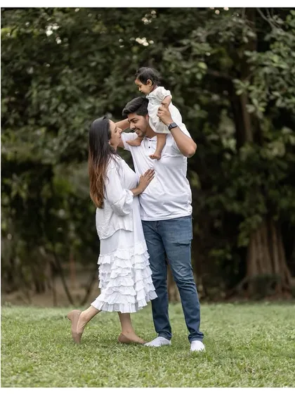 A beautiful family portrait taken outdoors, with the father lifting the baby onto his shoulders. A classic and heartwarming pose.