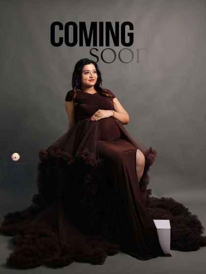 A hopeful and forward-looking portrait of the mother-to-be. Seated in an elegant brown gown, she gazes into the distance, with the words 'Coming Soon' hinting at the new arrival.