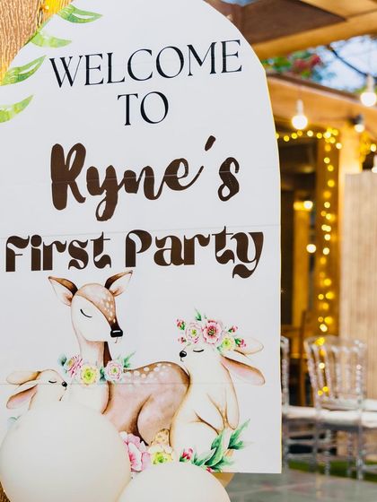 A close-up of the personalized welcome sign for "Ryne's First Party." The sign features beautiful illustrations of a deer and bunnies, perfectly matching the gentle woodland theme.