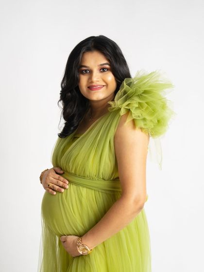 A close-up portrait showcasing a unique lime green tulle gown with a ruffled shoulder detail. The mother-to-be smiles gently, her hands cradling her baby bump.