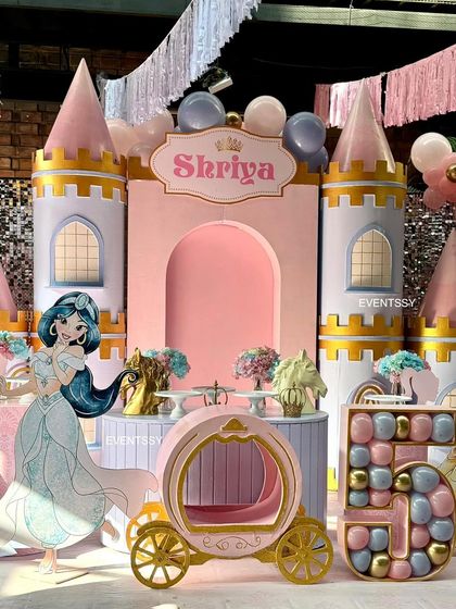A Disney Princess theme featuring a beautiful pink castle backdrop for Princess Shriya's 5th birthday. The setup includes a Princess Jasmine cutout, a royal carriage prop, and a balloon-filled marquee number "5."