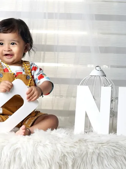 A happy one-year-old boy playing with "ONE" letter blocks on a fluffy white rug.