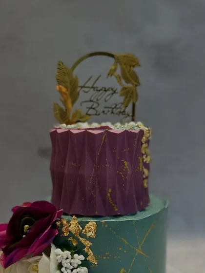 A close-up view focusing on the geometric texture of the purple top tier and the delicate gold leaf details. This highlights the precision and artistic touches I add to my modern cake designs.