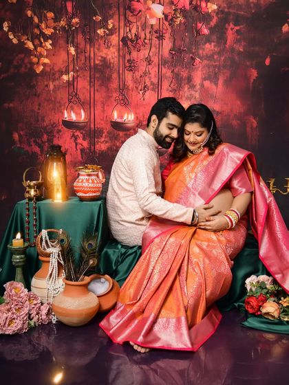 An intimate moment from a traditional maternity session. The couple is seated amidst earthen pots and diyas, with the mom-to-be glowing in a beautiful silk saree.