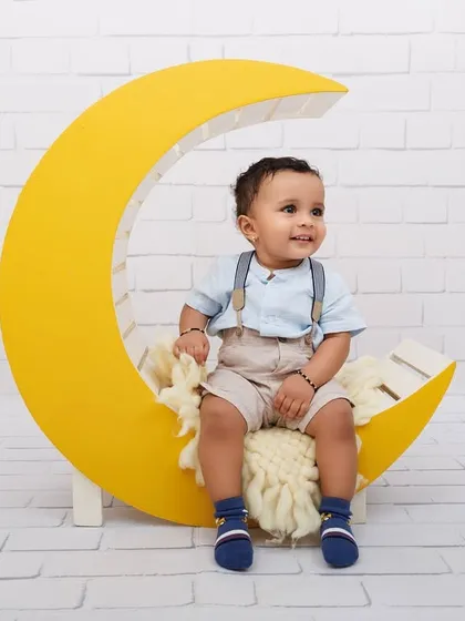 A smiling one-year-old boy enjoying his time on a yellow moon prop during his milestone session.