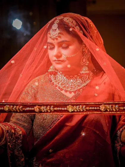 An atmospheric shot of a bride during a wedding ceremony, captured through her red veil.