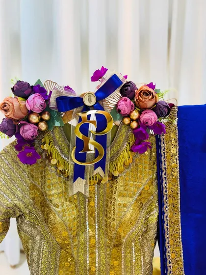 A close-up of the floral and initial detailing on the gold and blue outfit, showcasing the rich textures and colors.