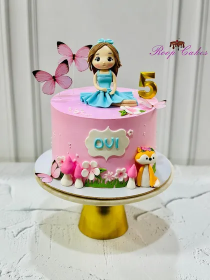 A pretty pink 5th birthday cake featuring a custom doll, a friendly fox, and a garden of mushrooms and flowers.