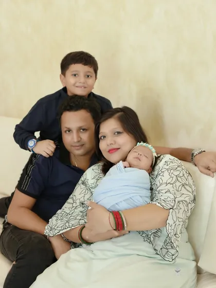 A happy family of four posing on a comfortable sofa. The mother cradles the newborn while the father and older son smile, creating a warm and relaxed family portrait.