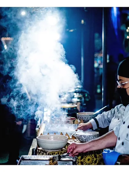 A dramatic, smoky shot of our live dosa station, capturing the sizzle and steam as the batter hits the hot plate.