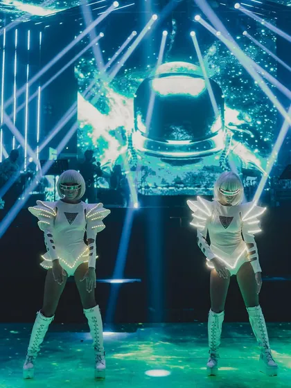 Dancers in futuristic white costumes with LED light strips perform on stage. The choreography and costumes were designed to perfectly match the event's space-age theme.